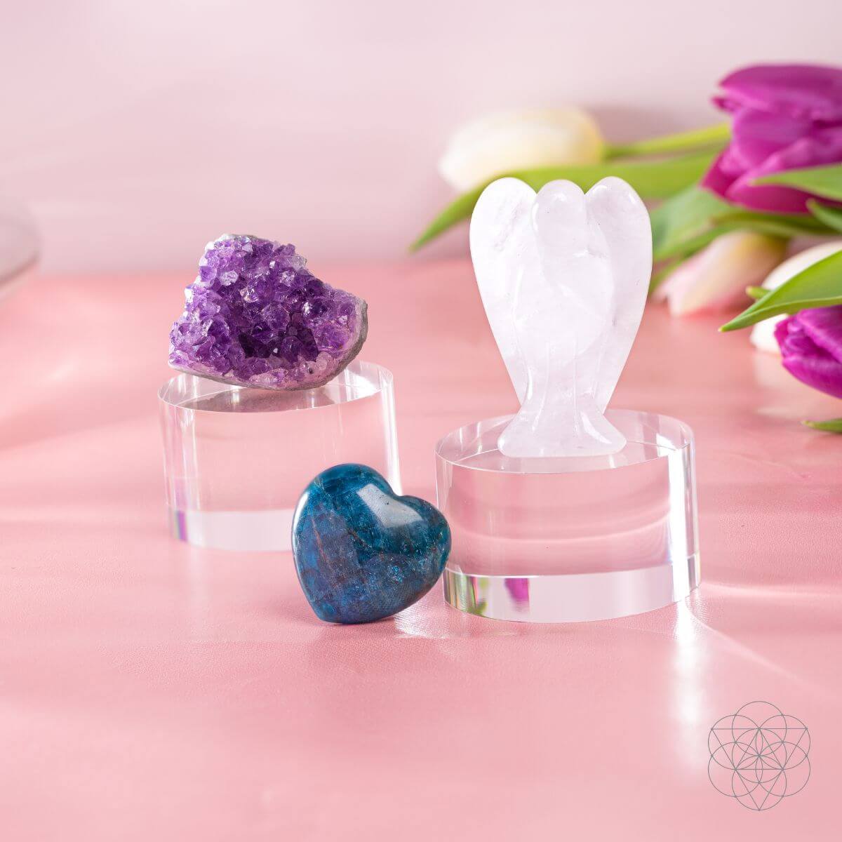 Amethyst cluster, Clear Quartz angel, and blue Apatite heart on clear display stands against a pink background.
