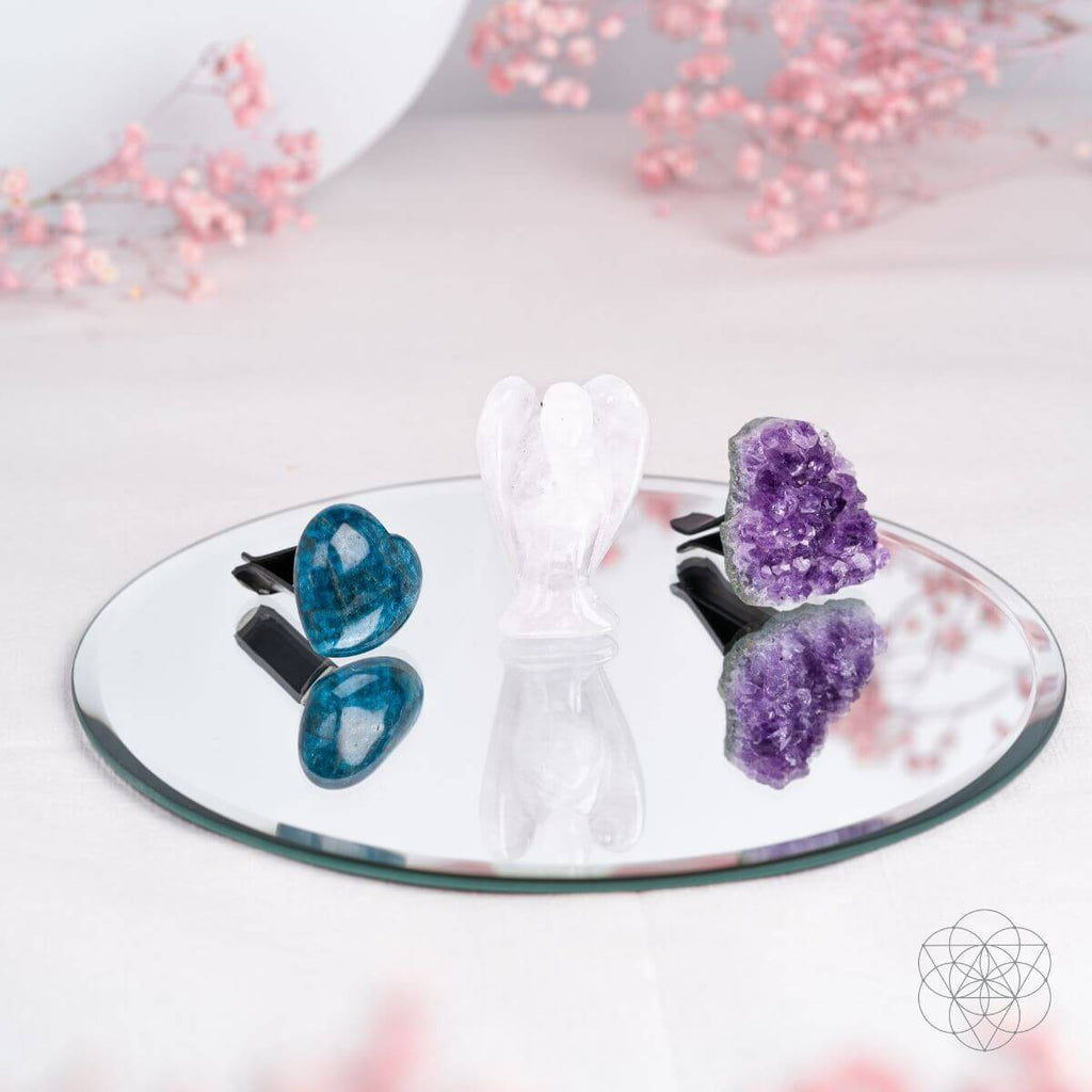 Three crystal car accessories on a round mirror with black vent clips visible behind the heart and cluster.