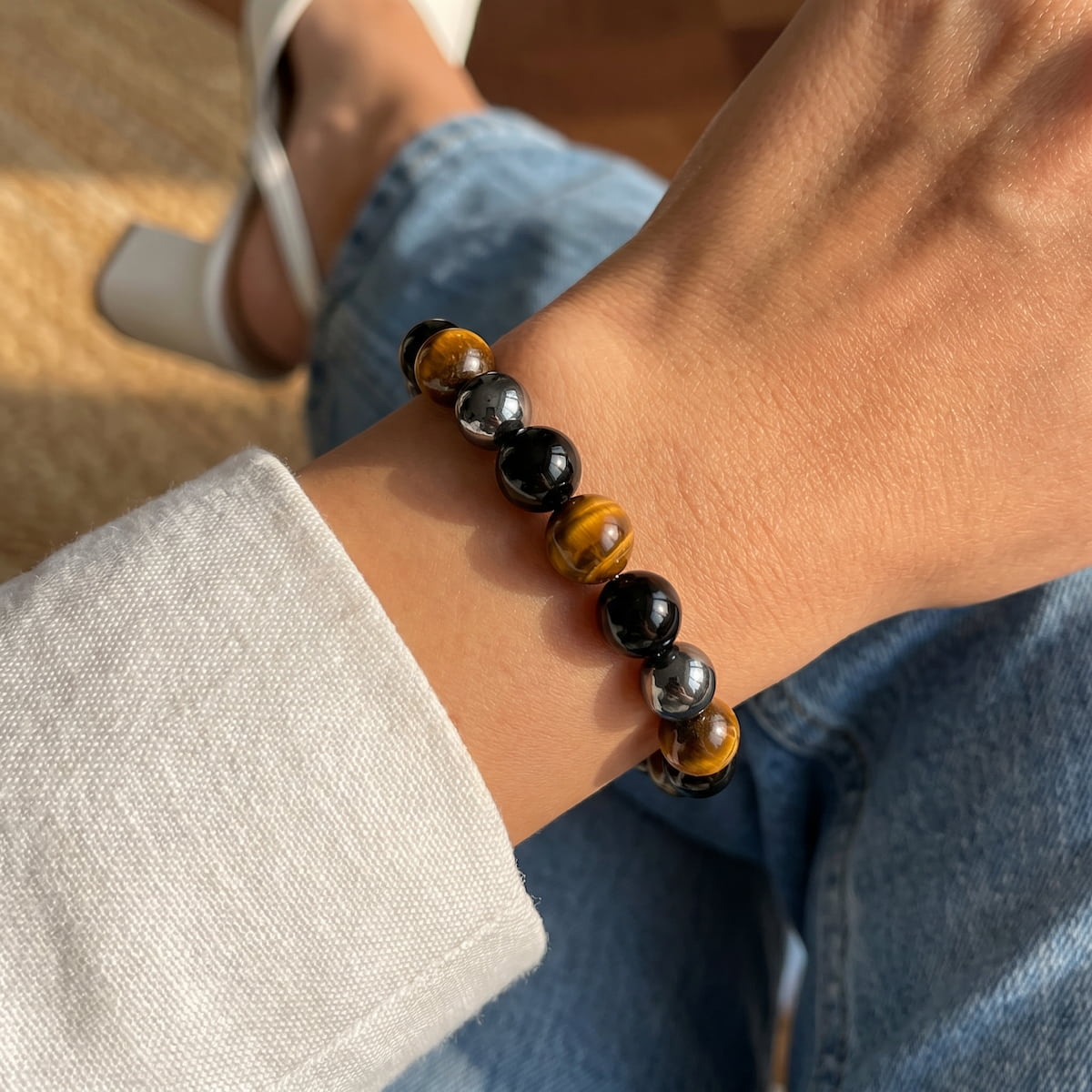 Close-up of golden-brown tiger’s eye, glossy black obsidian, and metallic-gray hematite beads on a wrist.