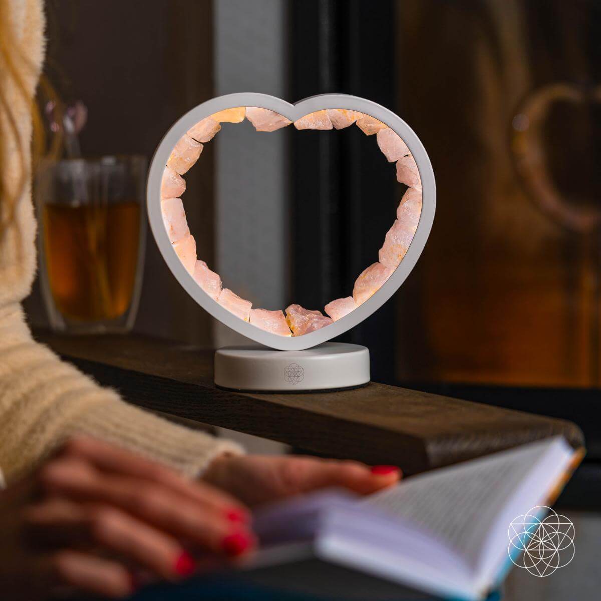 Small illuminated rose quartz heart lamp on a side table beside a person writing in an open notebook.
