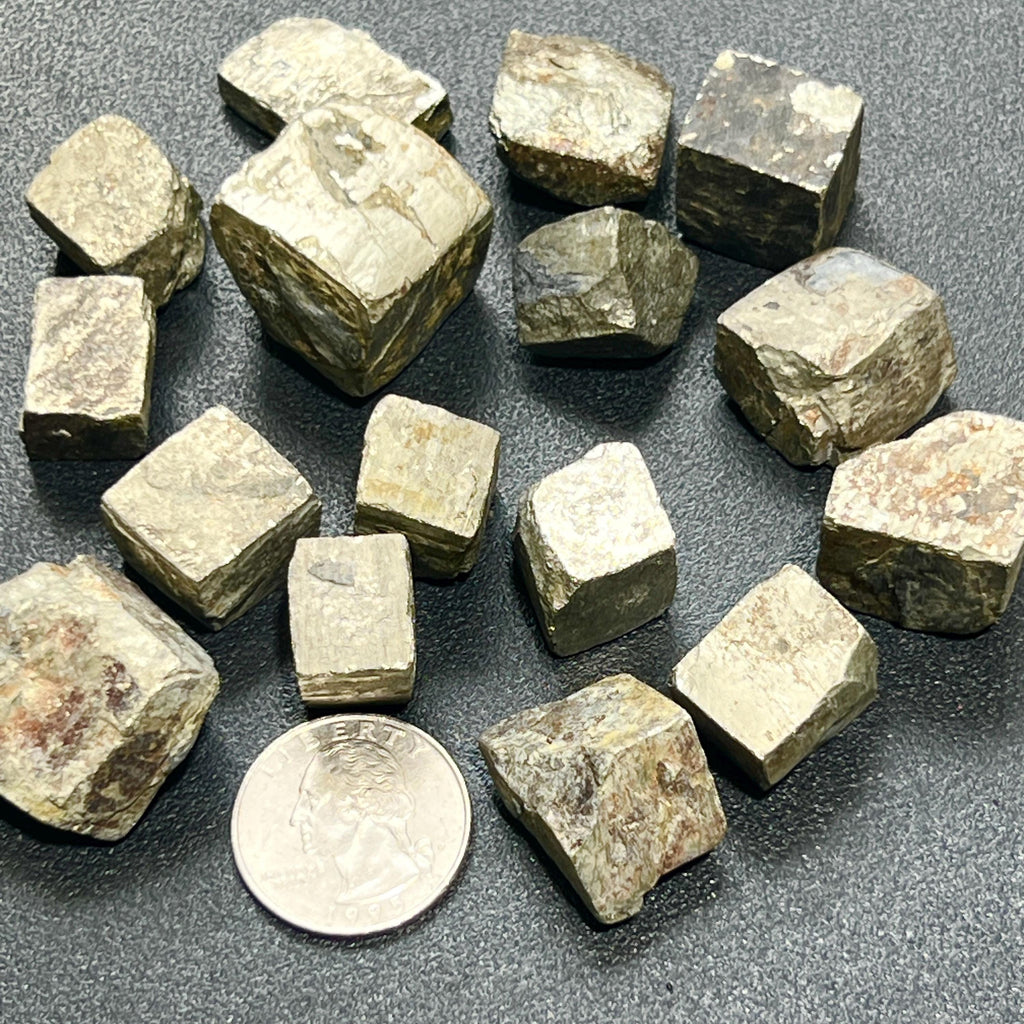 Small metallic iron pyrite crystal cubes arranged on a dark surface beside a quarter for scale