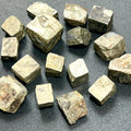 Assorted rough iron pyrite cubes with brass-gold faces, textured edges and varied block-like shapes on a dark surface