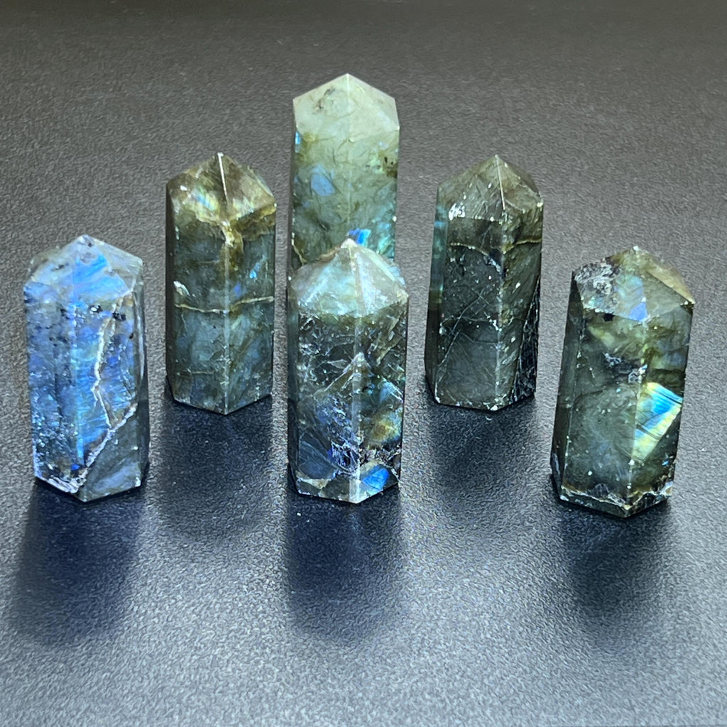 Six polished labradorite crystal towers with pointed tops and blue-green flashes standing on a dark surface