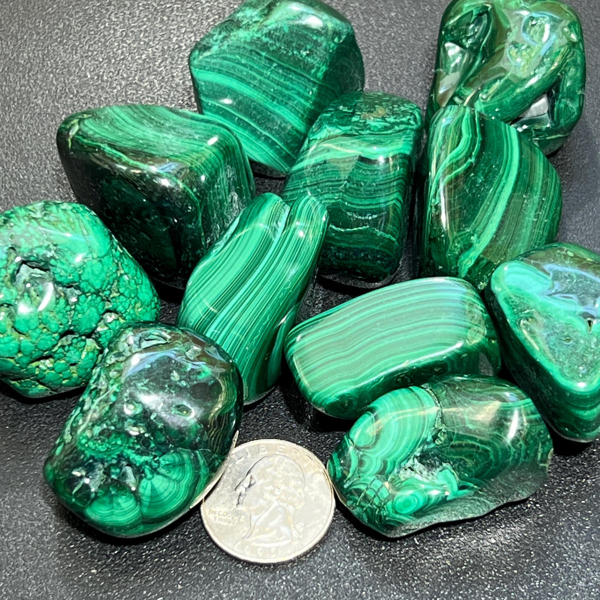 Assorted large green malachite tumbled stones with striped and circular patterns beside a quarter for size comparison.