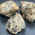 Three large rough black amber boulders with dark glossy patches and tan crust on a black surface