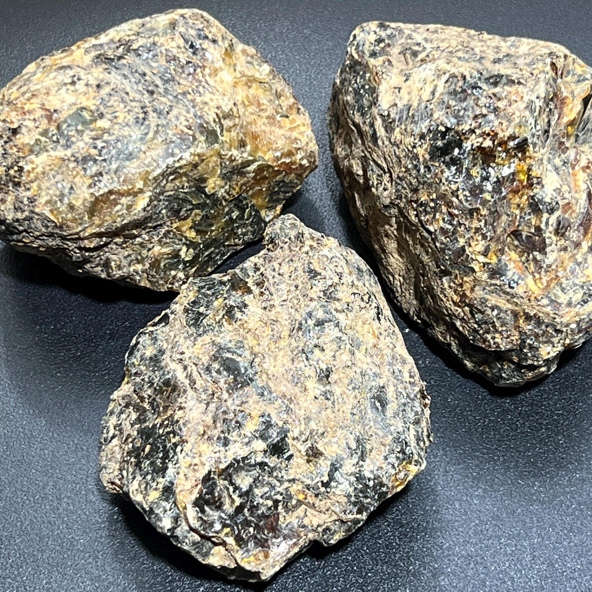 Three large rough black amber boulders with dark glossy patches and tan crust on a black surface