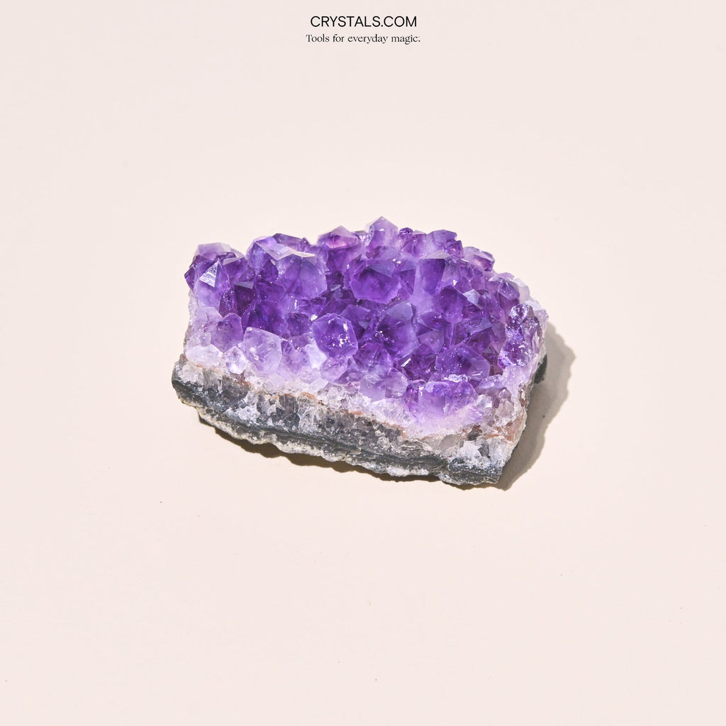 Broad lavender amethyst cluster showing large crystal points above a white quartz band and gray base.
