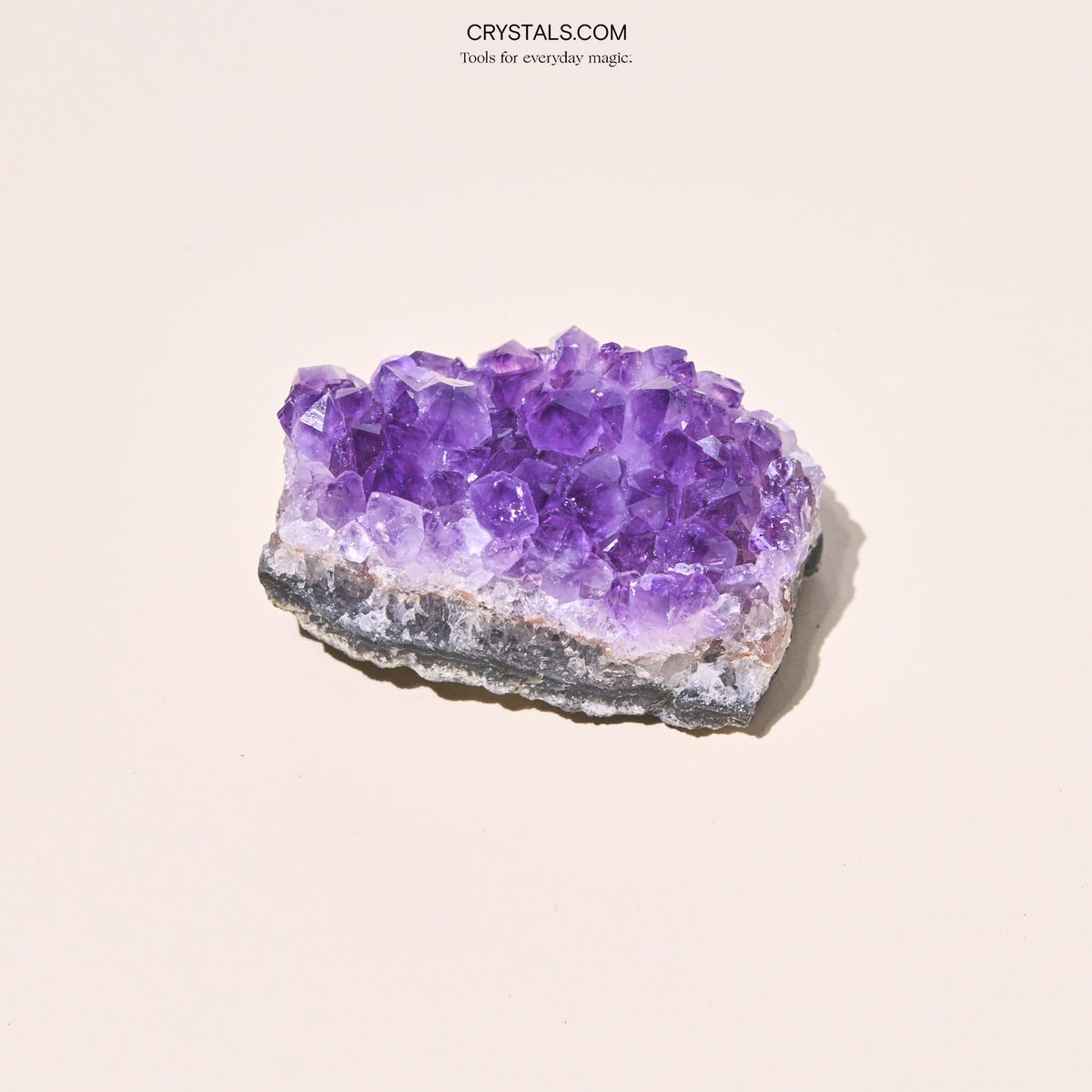 Broad lavender amethyst cluster showing large crystal points above a white quartz band and gray base.
