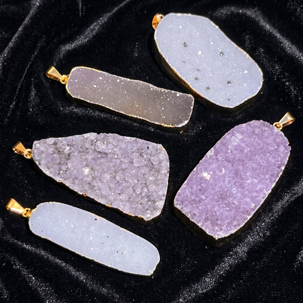 Five white, gray and lavender druzy crystal statement pendants with gold-plated borders on black velvet