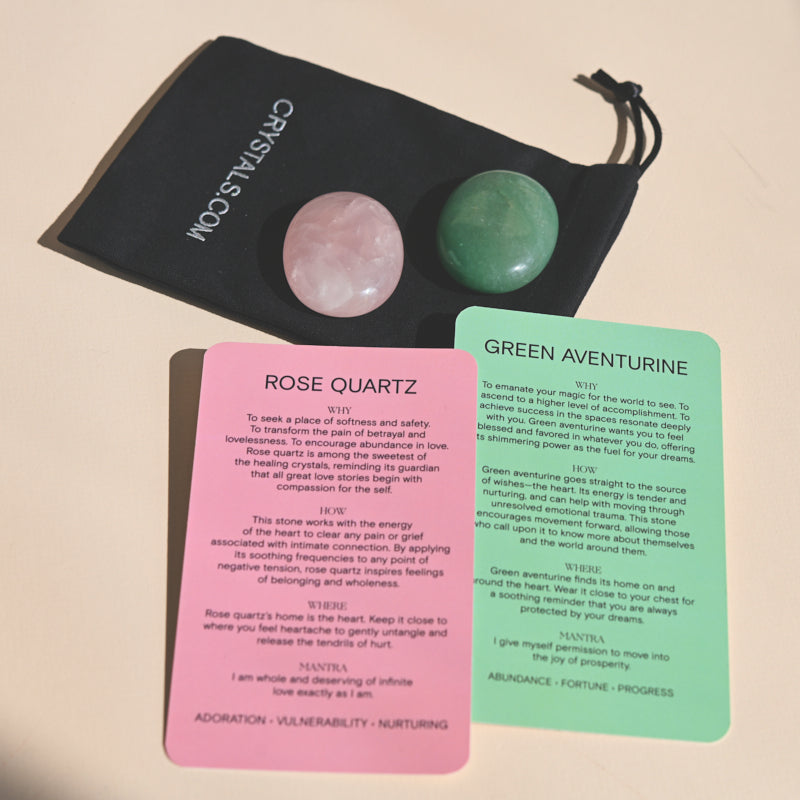 Rose quartz and green aventurine palm stones resting on a black pouch above pink and green information cards.
