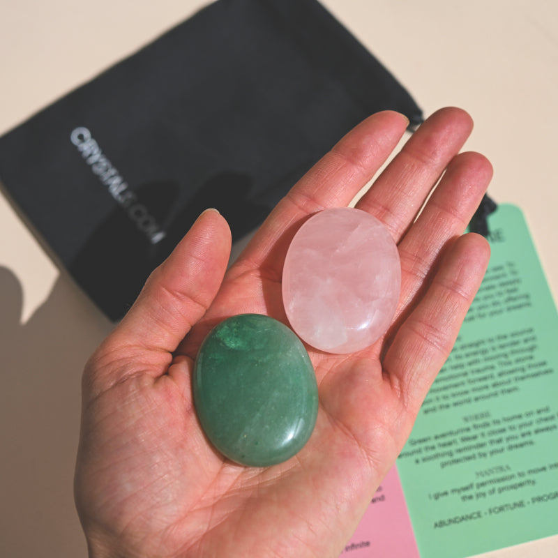 Open hand holding a pink rose quartz palm stone and a green aventurine palm stone.
