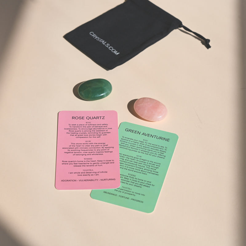 Overhead view of a black pouch, pink rose quartz and green aventurine stones, and matching colored information cards.
