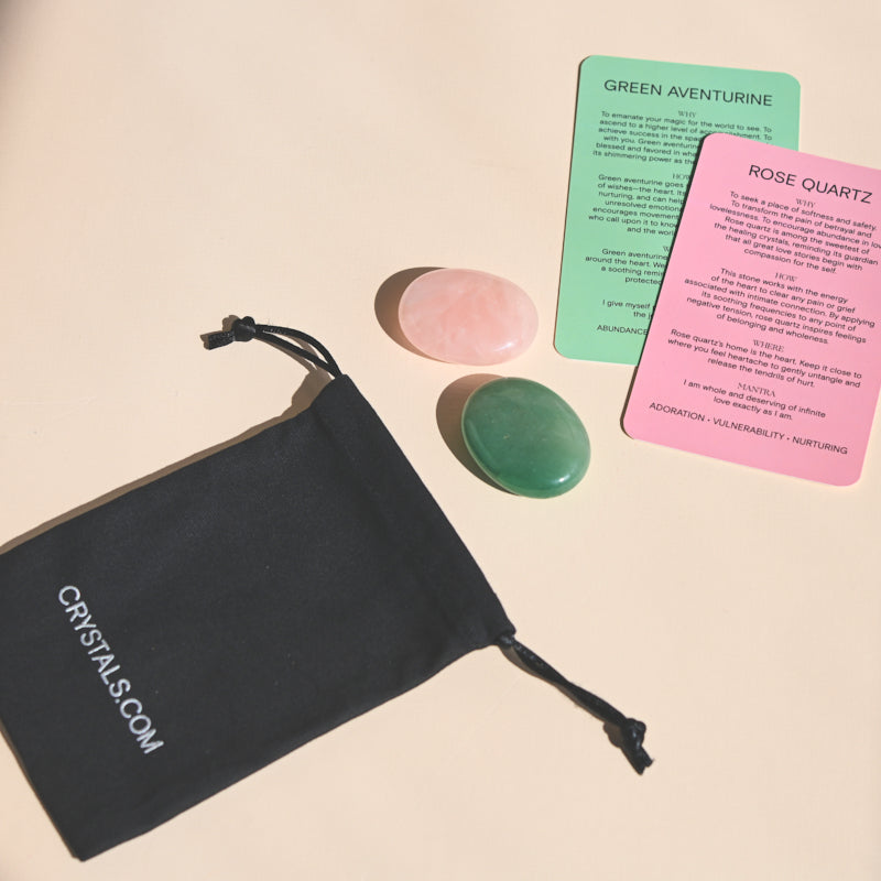 Pink rose quartz and green aventurine palm stones beside a black drawstring pouch and two information cards.
