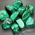 Large polished malachite tumbled stones with bright and dark green bands, curves, and ring patterns on a dark surface.