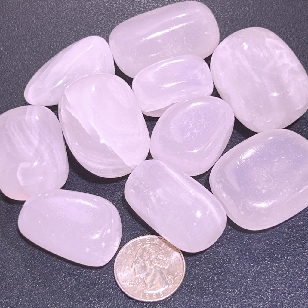 Pale pink polished mangano calcite stones with subtle white bands beside a quarter for size comparison.