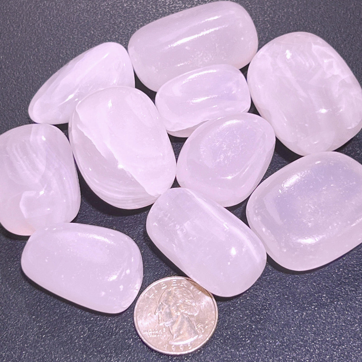  Pale pink polished mangano calcite stones with subtle white bands beside a quarter for size comparison.
