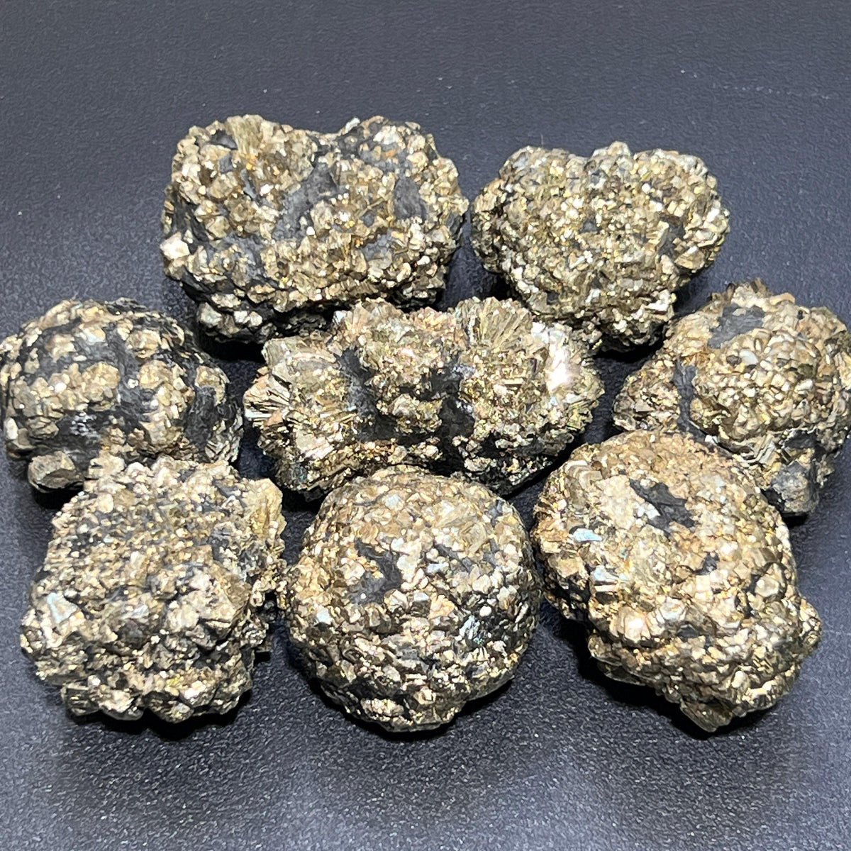 Eight irregular marcasite pyrite crystal nodules showing brass-gold clusters and dark patches on a black background