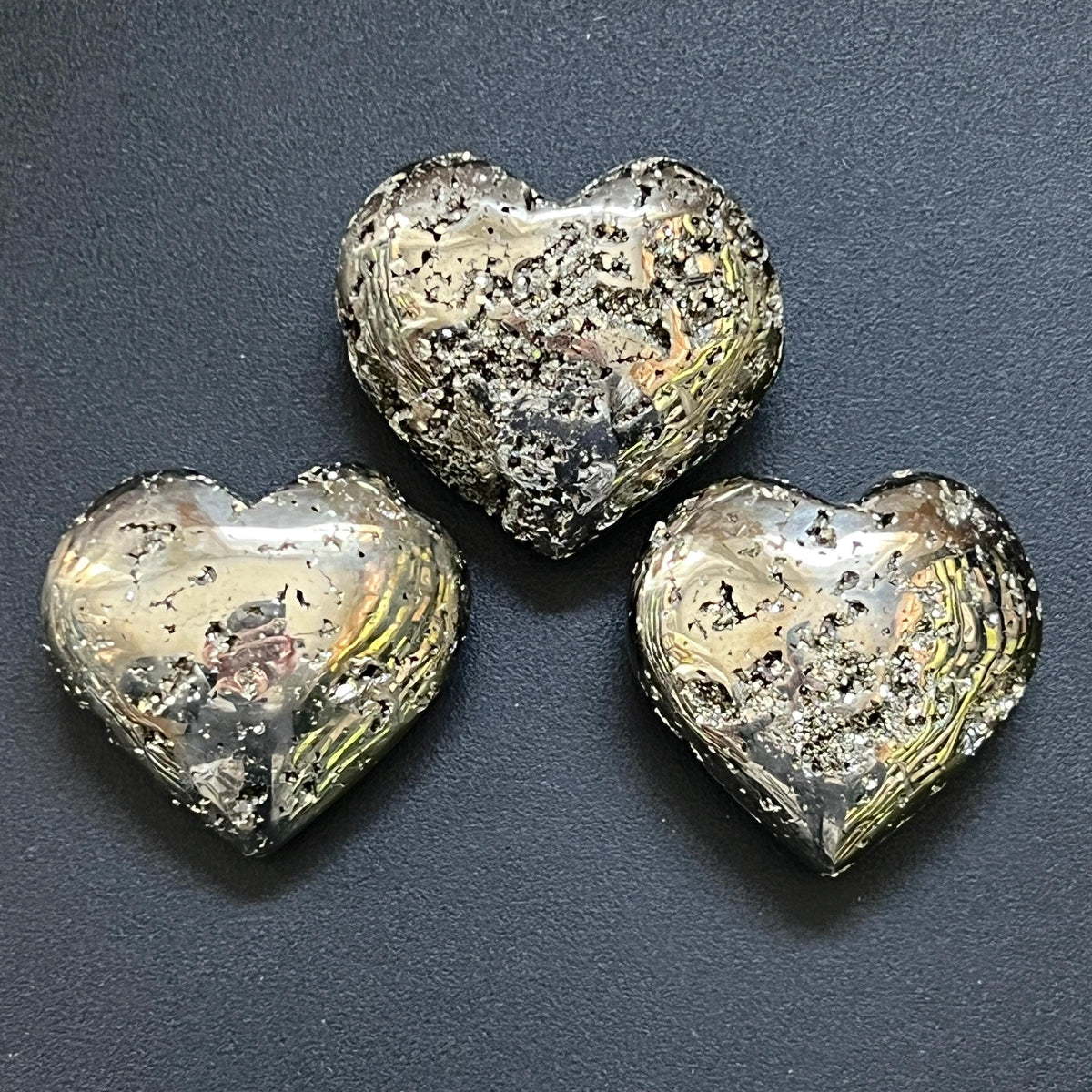 Three metallic pyrite puffy heart carvings with polished surfaces and druzy crystal pockets on a dark background.