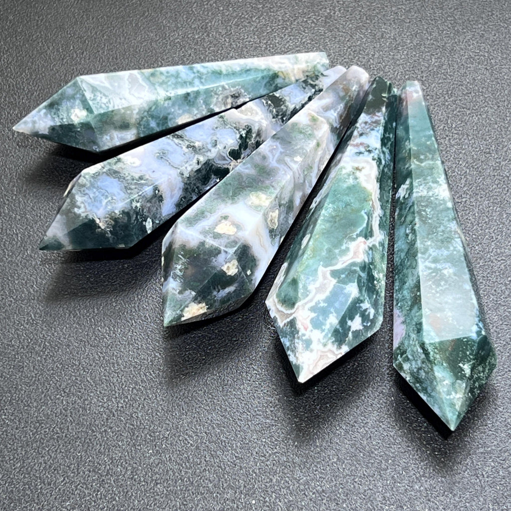 Five faceted moss agate scepter wands with green and white patterns arranged in a fan on a dark surface.
