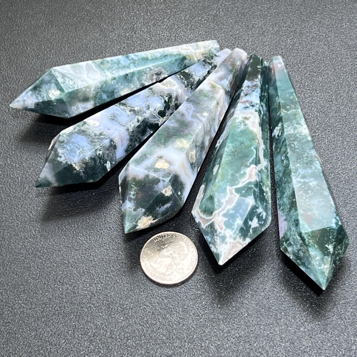Five pointed moss agate scepter wands with green, white, and translucent areas beside a quarter for size comparison.
