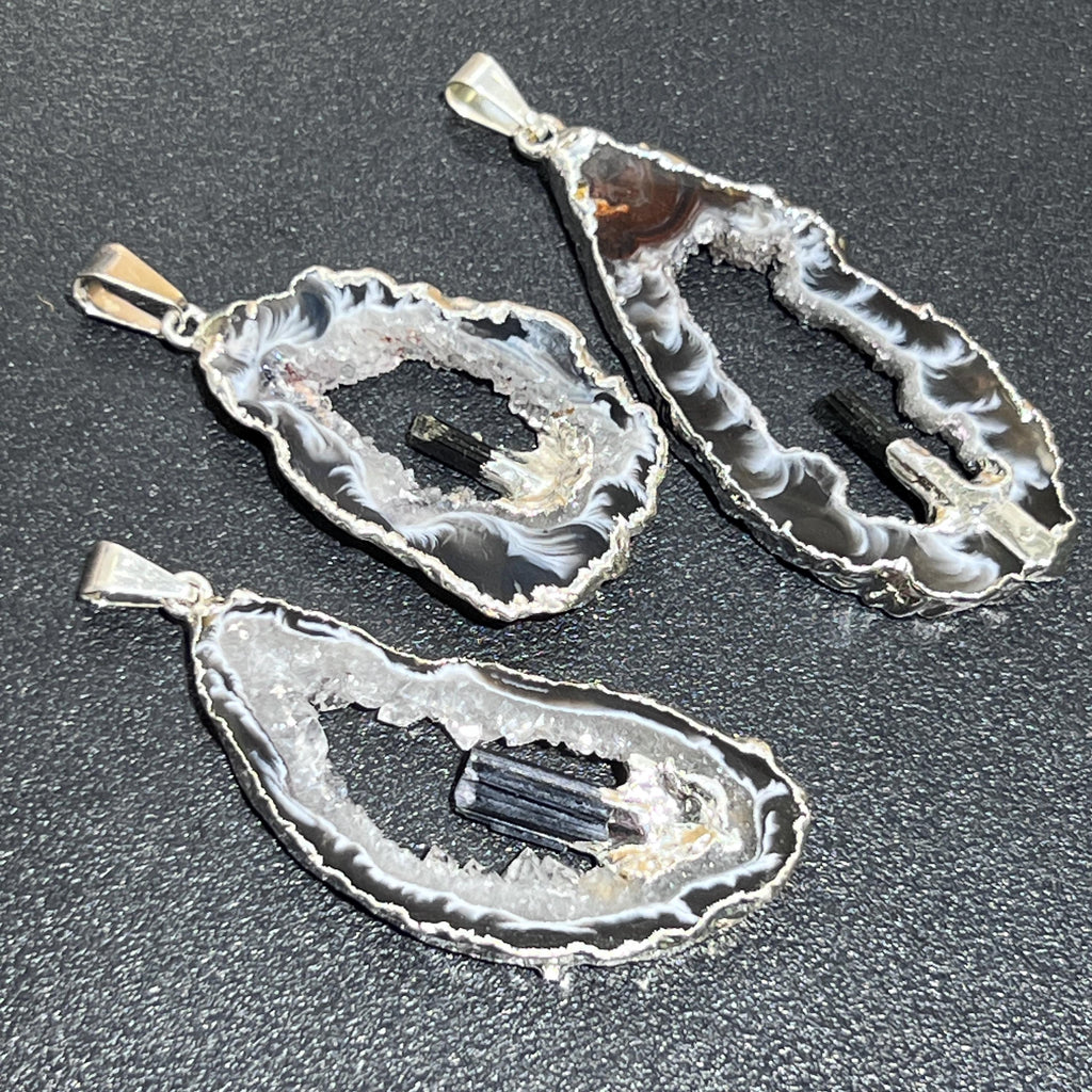 Close-up of three open-center geode pendants showing white crystal linings, gray bands and black tourmaline crystals