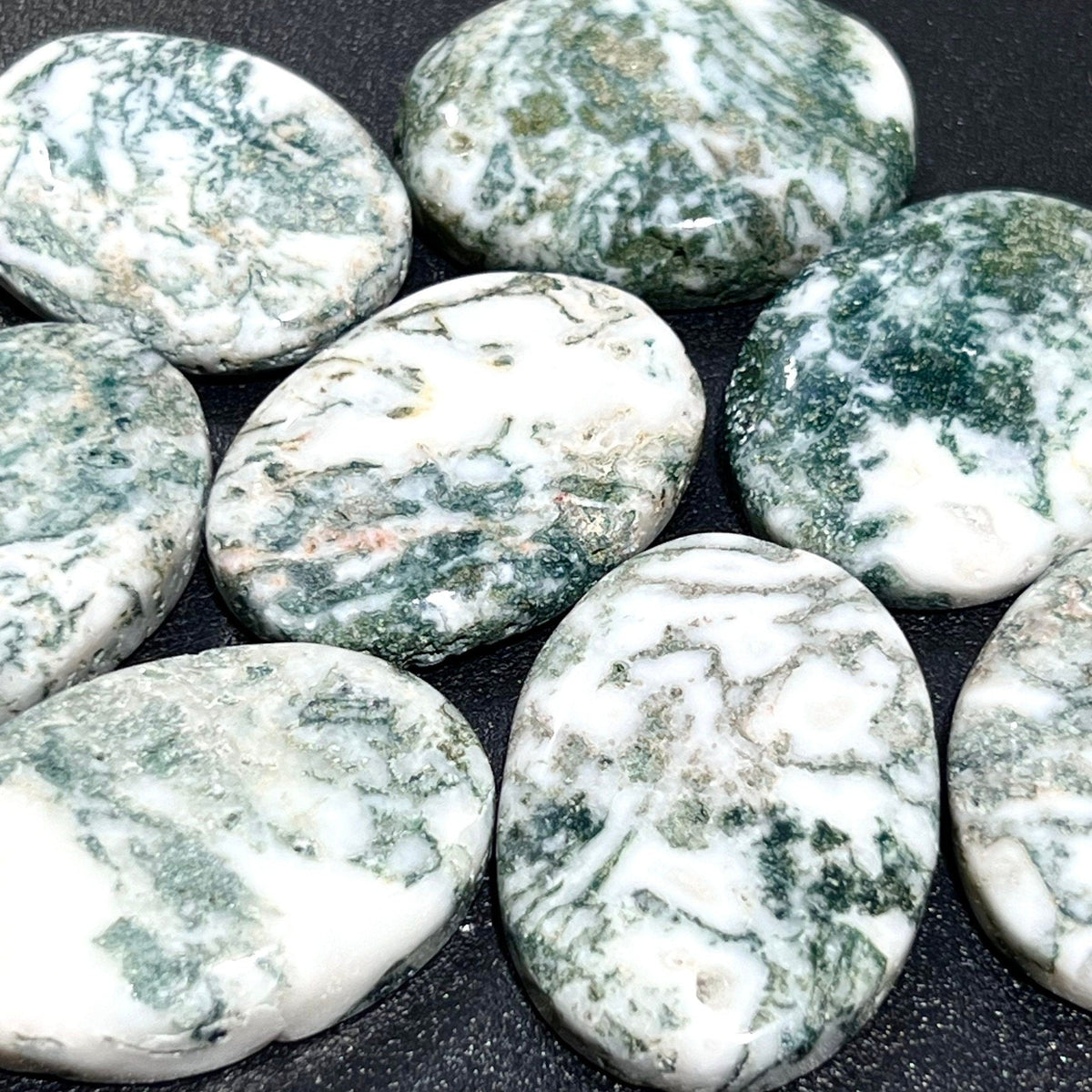 Detailed view of oval tree agate cabochons with mossy green markings across glossy white surfaces.