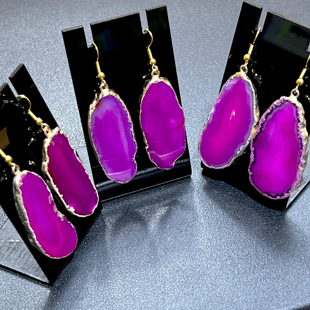 Angled view of pink agate slice dangle earrings showing pale banding and irregular gold-plated edges on black stands.