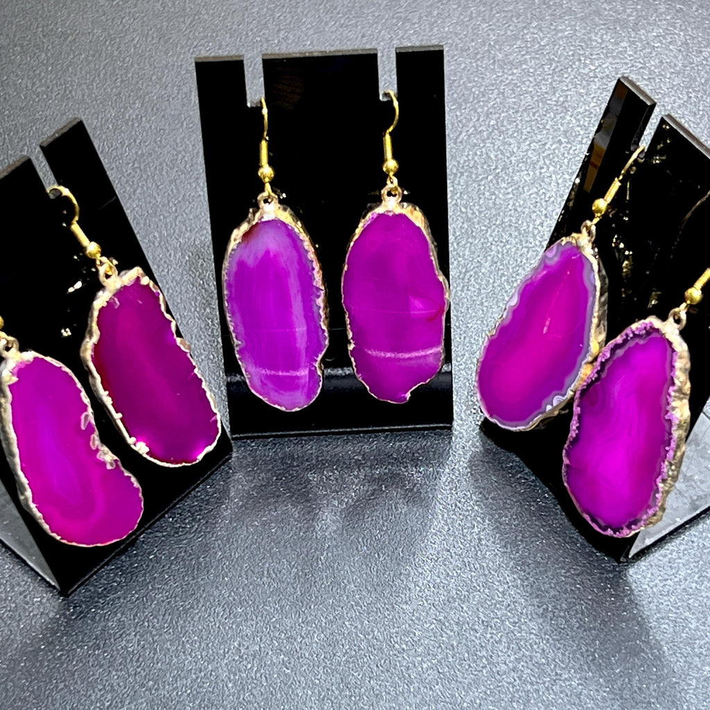  Three pairs of vivid pink agate slice earrings with gold-plated edges and gold-colored hooks on black display stands.