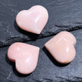 Three polished pale pink opal puffy heart carvings arranged on dark layered slate.