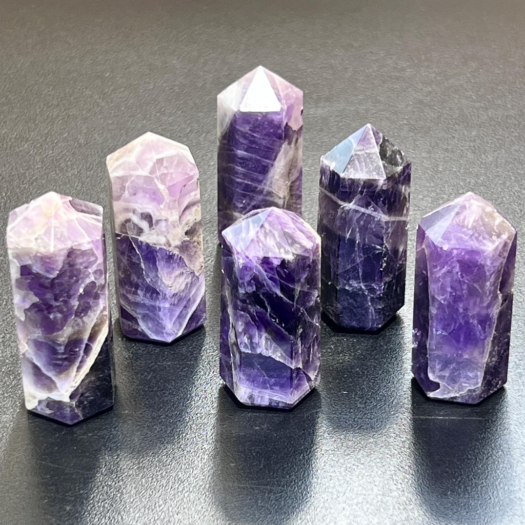 Six polished amethyst towers showing varied purple shades and white bands against a dark background