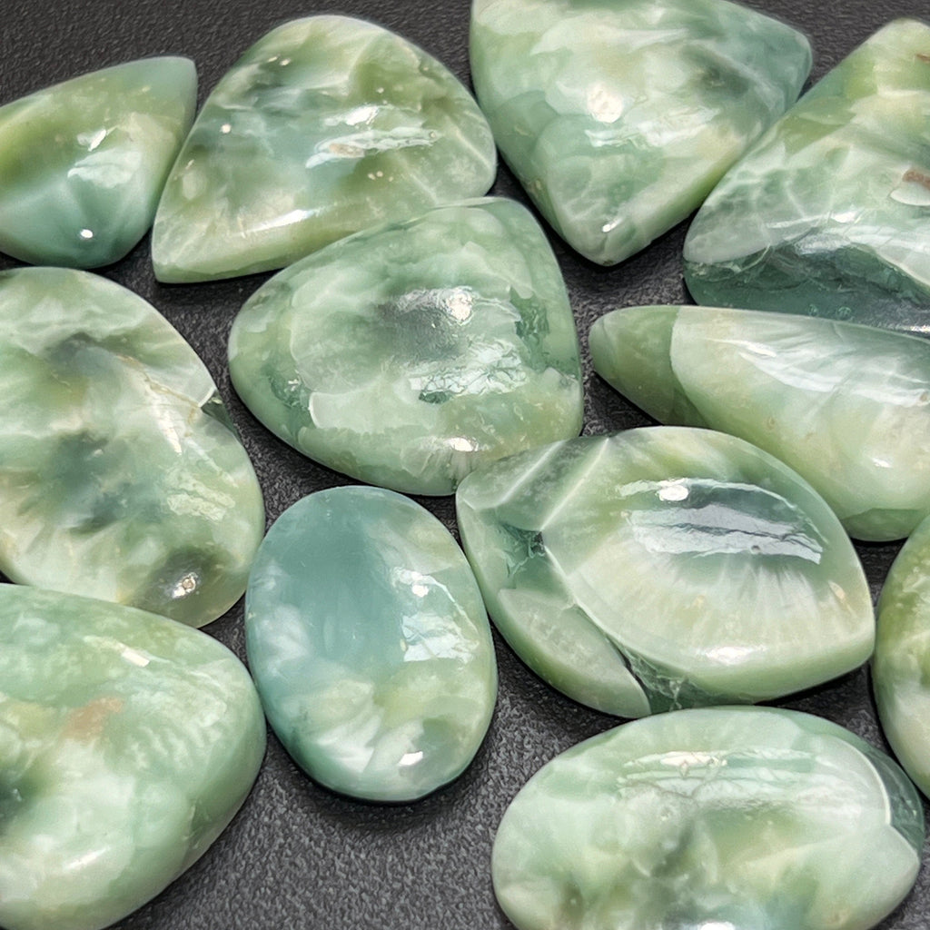 Close-up of polished green hemimorphite cabochons with pale mottled patterns in assorted oval and teardrop shapes