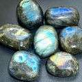 Seven polished labradorite palm stones showing blue, turquoise, green and gold flashes on a dark surface