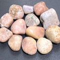Group of polished pink amethyst tumbled stones in blush, peach and pale lavender tones on a dark surface