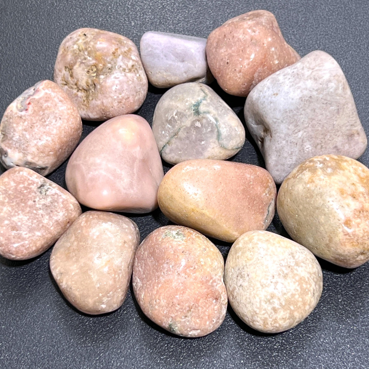 Group of polished pink amethyst tumbled stones in blush, peach and pale lavender tones on a dark surface