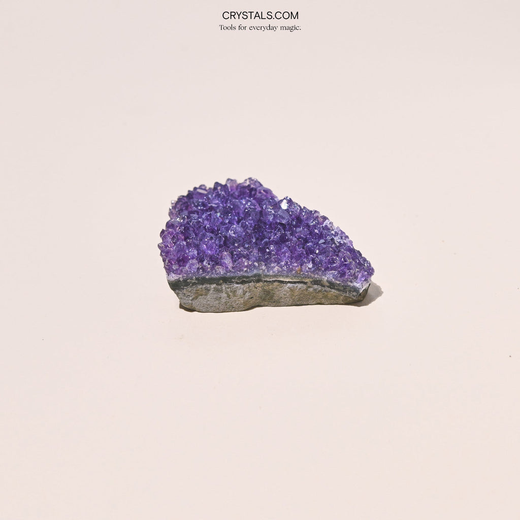 Side view of a compact purple amethyst cluster showing its thick rough stone base.
