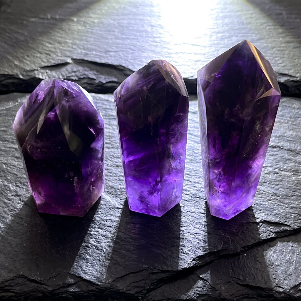 Three dark purple amethyst crystal towers arranged by height on layered black slate