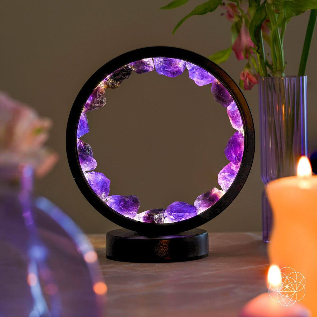 Lit purple amethyst halo lamp displayed on a table beside candles and a vase of flowers.
