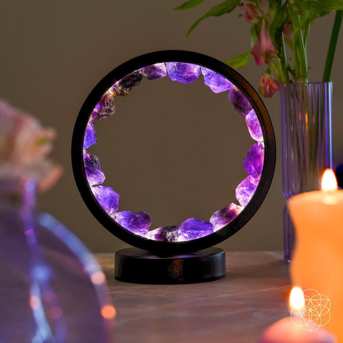 Lit purple amethyst halo lamp displayed on a table beside candles and a vase of flowers.
