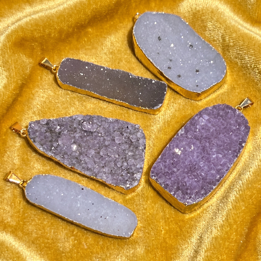 White, gray and purple druzy crystal pendants in varied shapes with gold-plated edges on golden fabric
