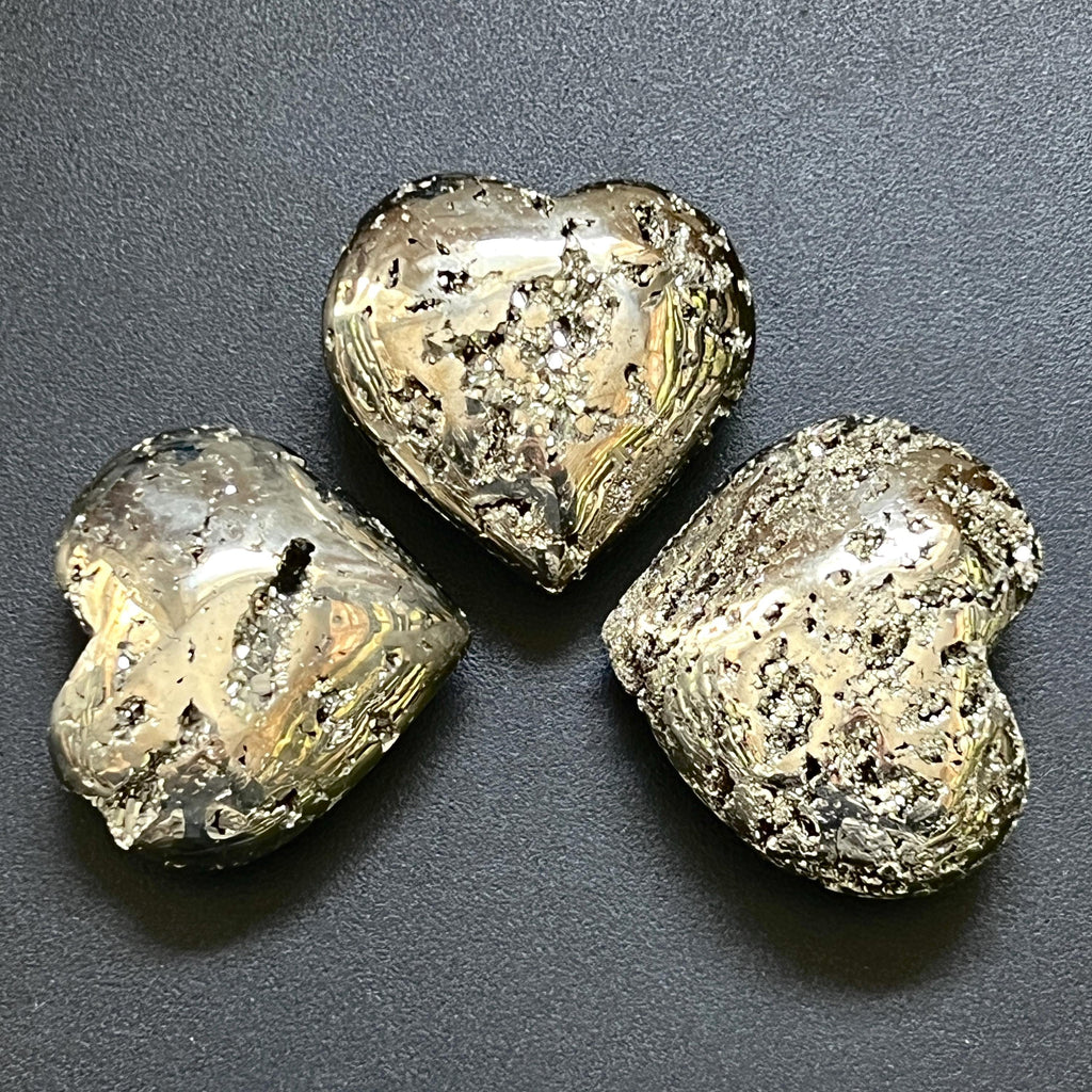 Three pyrite druzy hearts at different angles showing rounded thickness and contrasting smooth and crystal-textured areas.
