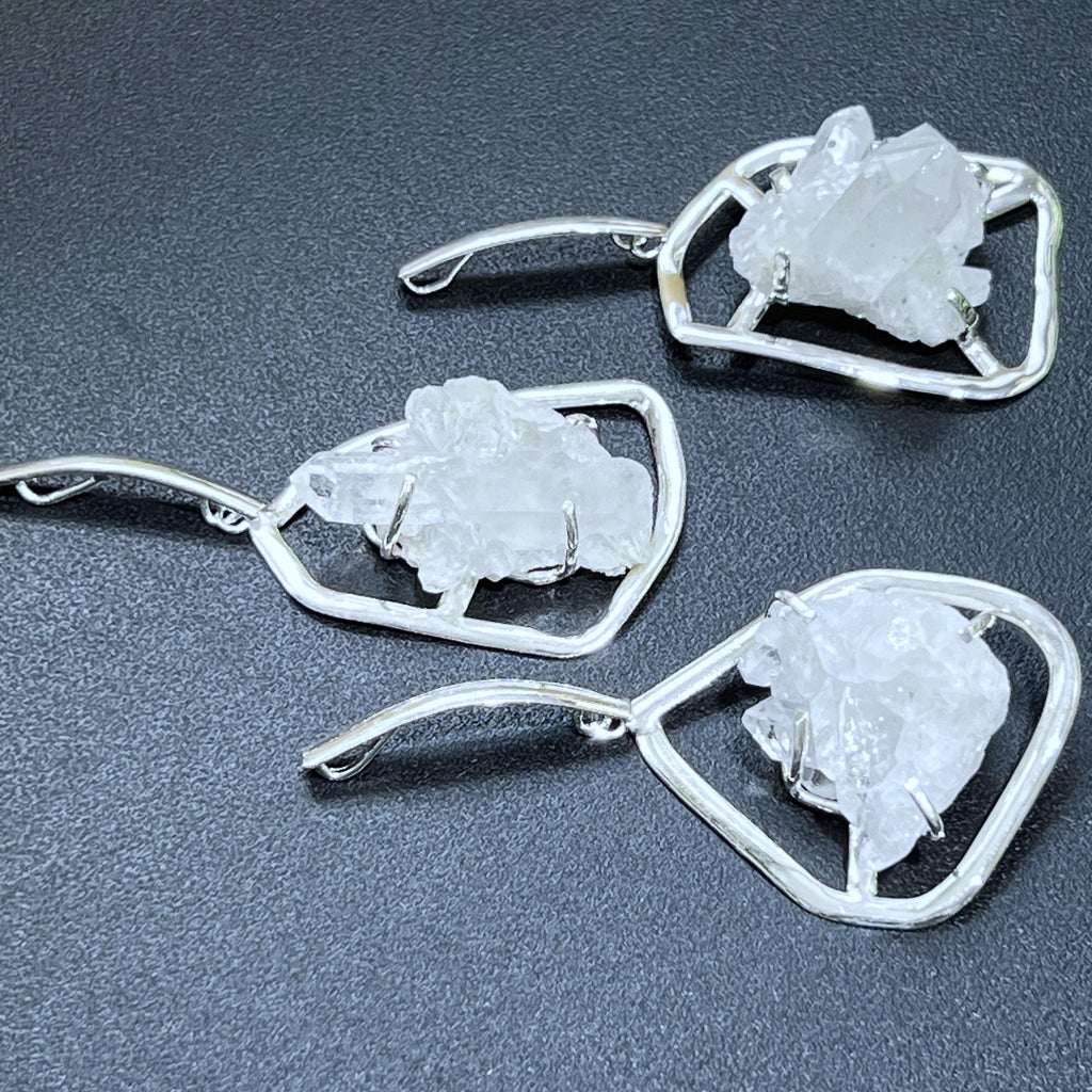 Close-up of three quartz cluster pendants showing crystal points and silver-plated prong supports on a dark background.
