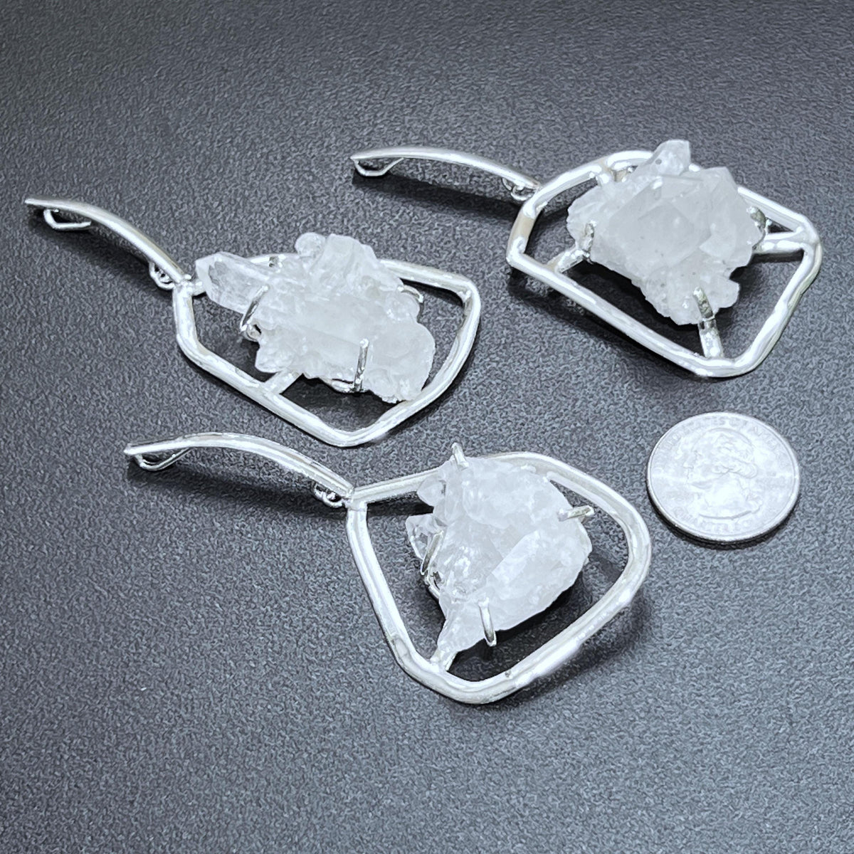 Three silver-plated quartz cluster statement pendants beside a quarter for size comparison on a dark surface.
