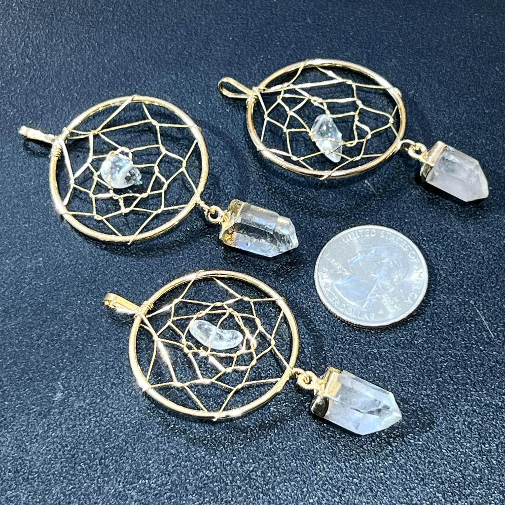 Three gold-plated quartz dreamcatcher pendants on a dark surface beside a quarter for size comparison.
