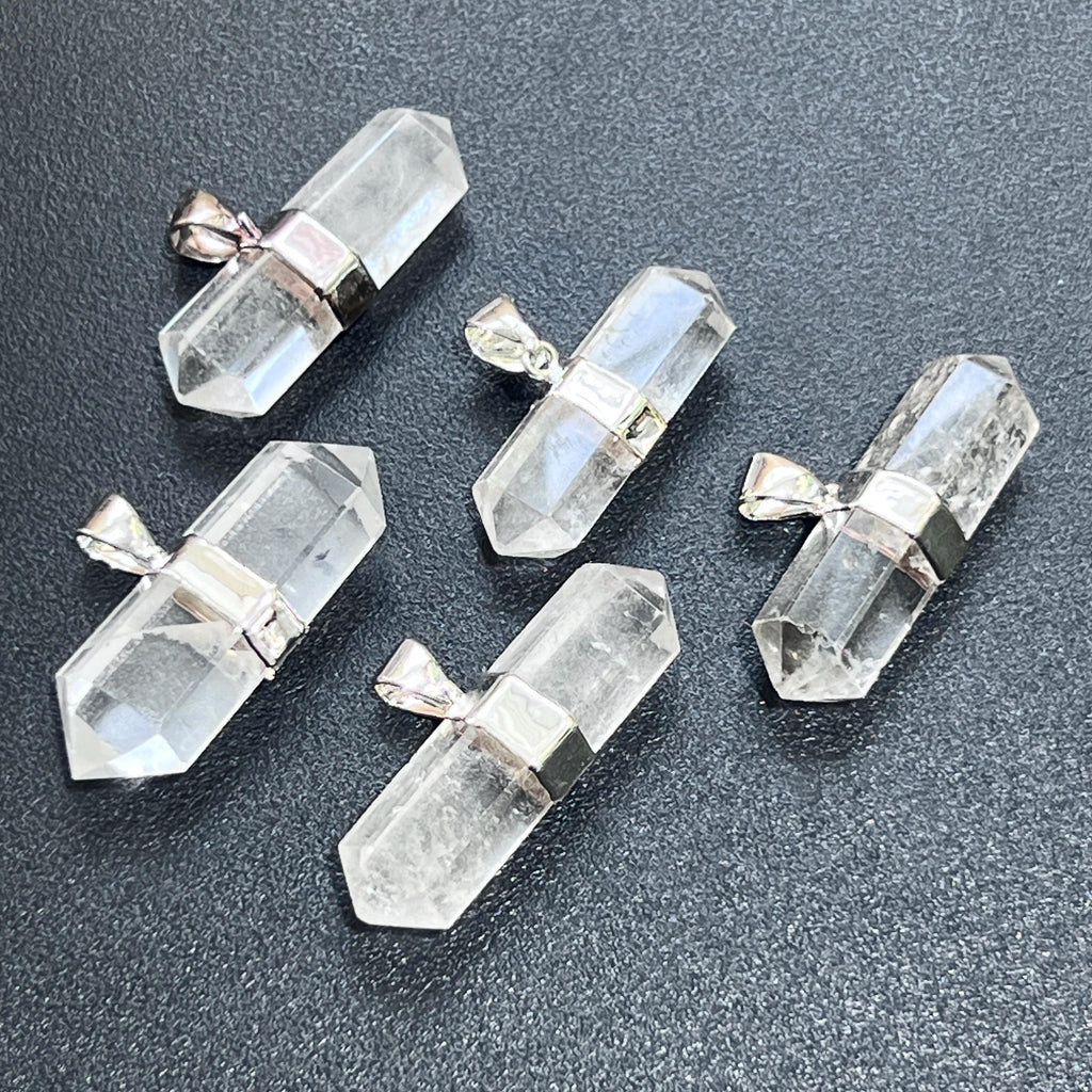 Five faceted double-terminated clear quartz pendants with silver-plated center bands and hanging bails on a dark surface.

