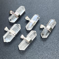 Five faceted double-terminated clear quartz pendants with silver-plated center bands and hanging bails on a dark surface.
