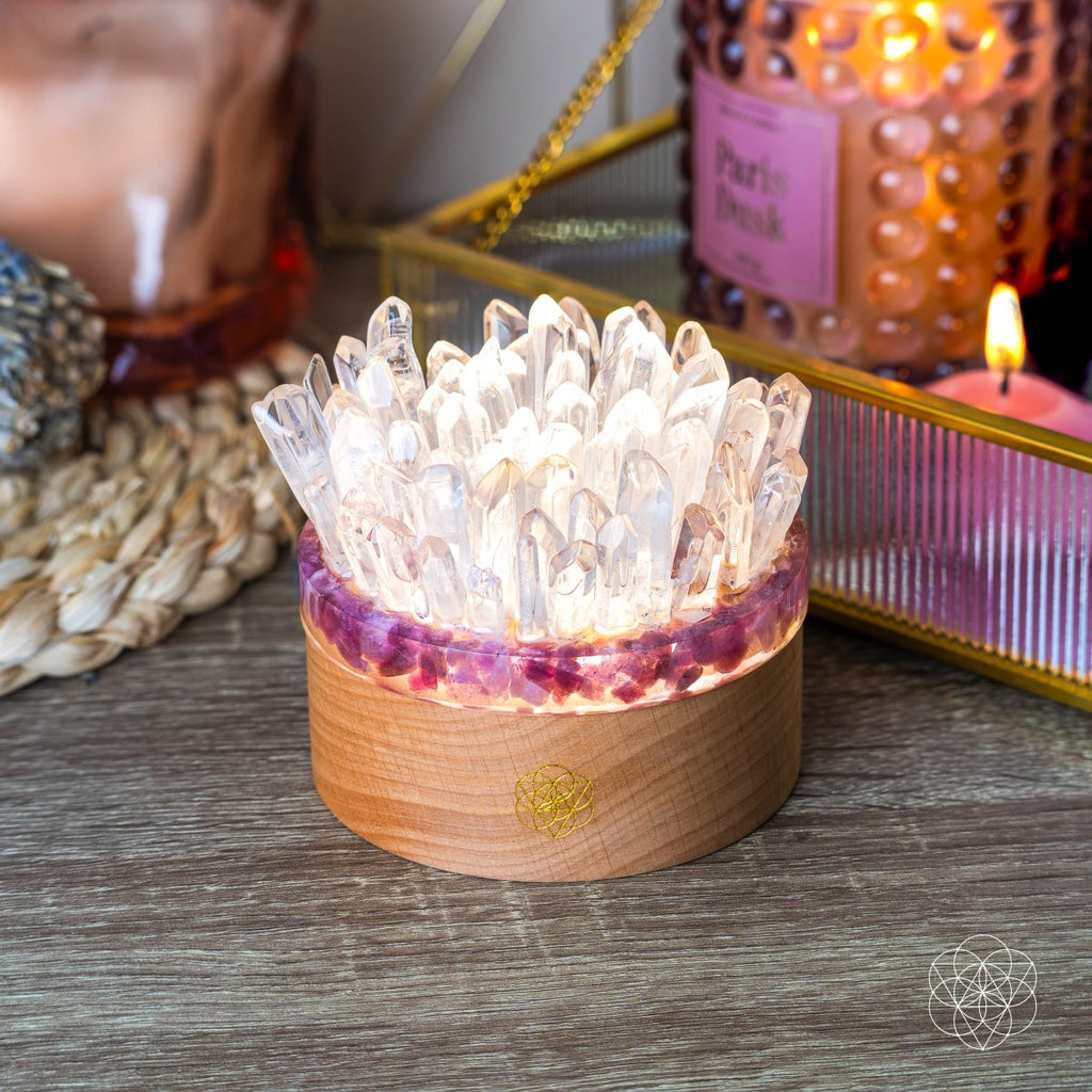 Angled view of a bright quartz point lamp with a pink stone band on a wooden base beside a mirrored tray.
