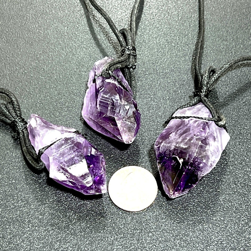 Three raw amethyst point necklaces with black cords beside a coin for size comparison.