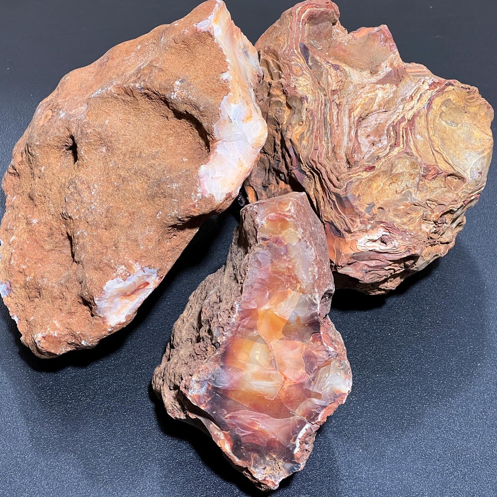 Close-up of three raw carnelian agate boulders showing rugged brown textures and orange and cream interiors