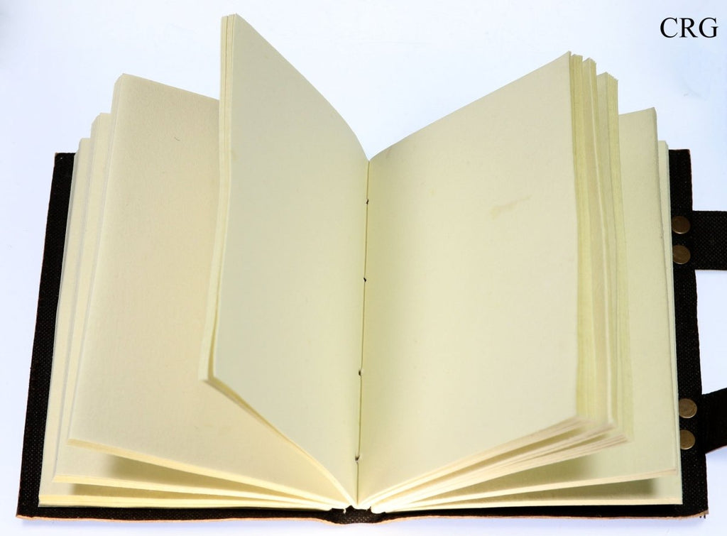 Leather journal opened to blank cream parchment pages with stitched center binding