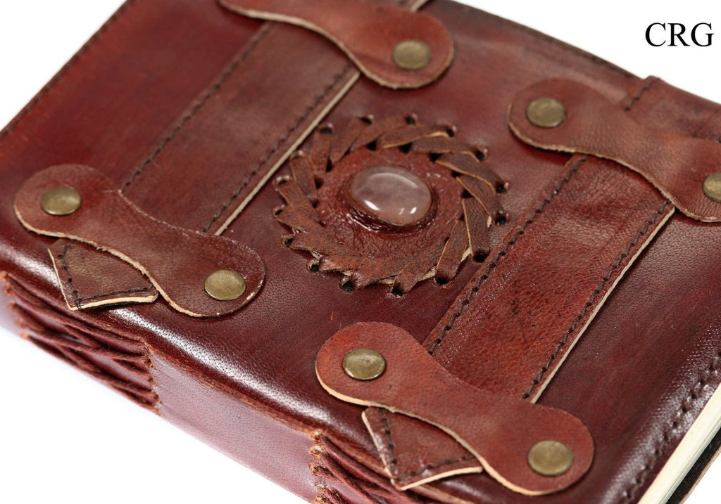 Angled close-up of rose quartz leather journal showing the stone accent, decorative straps and stitched spine